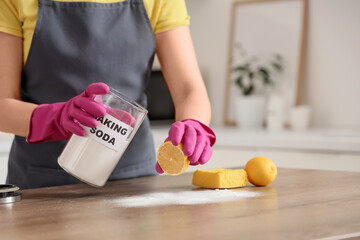 Young woman with lemon and baking soda cleaning table in kitchen, closeup
