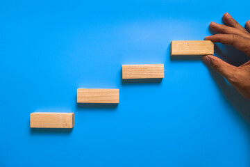 male hand put stairway wooden blocks isolated on blue background
