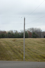 A wooden utility pole with power lines by a grassy field in autumn
