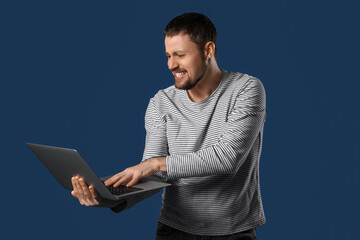 Screaming young man using laptop on dark blue background
