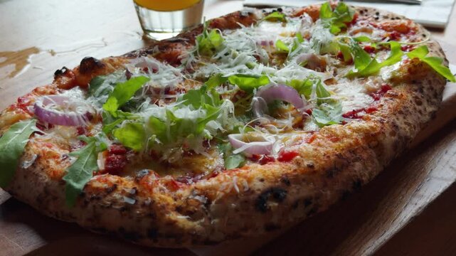 An overhead, mouth-watering shot of a hot, freshly baked gourmet pizza. The toppings include vibrant rocket salad, savory meat, and perfectly melted mozzarella cheese bubbling across the crust. 