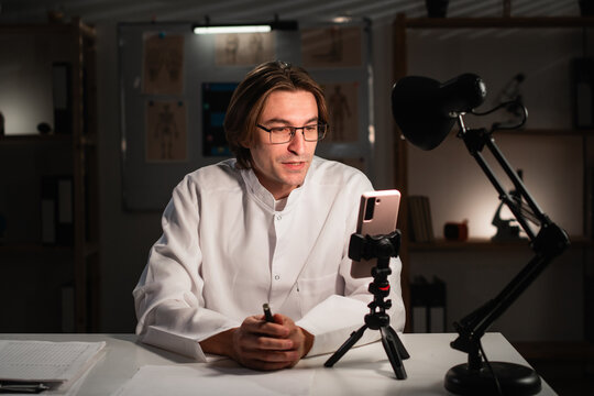 doctor with glasses using mobile phone camera recording video for followers in social media. Medicine and blogging