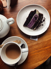 Close-up of a half-drunk cup of coffee and a slice of cake served on white crockery, with a white teapot and sugar sticks nearby. A visible QR code on the rustic wooden table.