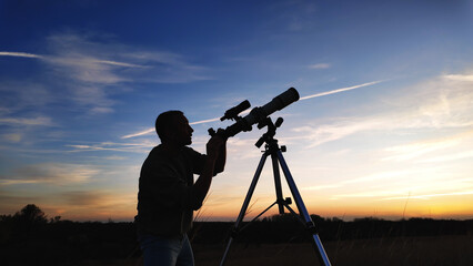 Silhouette of an amateur astronomer using telescope for observing stars, planets, Moon and other celestial objects.