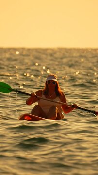 Kayaking woman sunset paddling orange kayak on ocean water during golden hour leisure vacation activity Vertical video