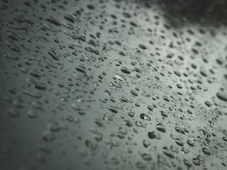 Close-up view of raindrops on a car window during a rainy day. Water droplets create a soft abstract pattern with reflections and blurred lights outside. Perfect for backgrounds, weather concepts