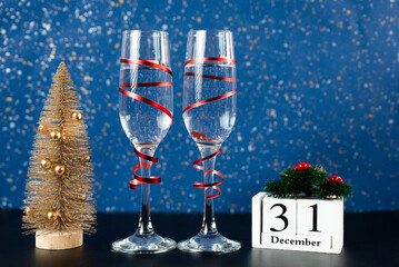 Elegant festive setup with champagne glasses, golden Christmas tree, and 31 December calendar on blue background. Great for New Years visuals. 