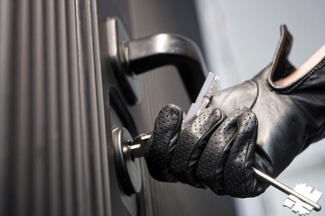 Close-up of a person in black leather gloves unlocking armored door with key, concept of burglary, break-in, or illegal entry. Photo