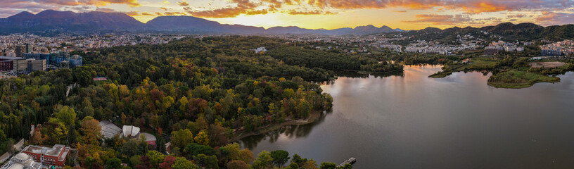 Obraz premium Aerial panorama of Tirana’s Artificial Lake and Grand Park at sunrise, glowing with golden light and autumn colors.