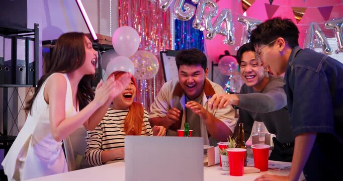 Diverse group of young Asian coworkers react with joy to exciting news on a laptop screen. A vibrant office moment filled with teamwork, success, celebration, and high-energy emotion.