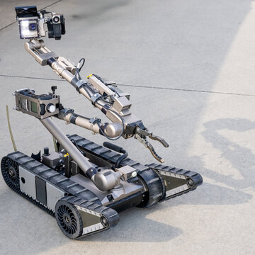 A high-tech bomb disposal robot equipped with cameras and articulated arms, designed for hazardous tasks, standing on a concrete surface during a field operation.