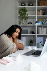 Sick latina freelancer working from home office with tissues and laptop