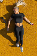Woman rests after outdoor workout on vibrant yellow surface with fitness gear.