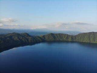 Fototapeta premium Drone aerial of deep blue mountain lake bordered by lush forested ridges under clear sky