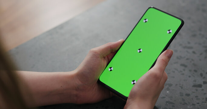 Young woman sitting at a counter and using smartphone with green screen