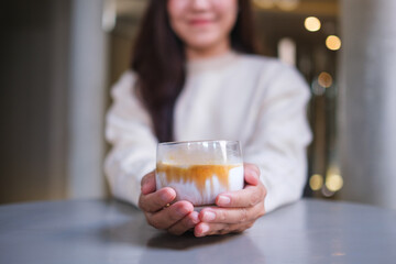Closeup image of a woman holding and serving a glass of dirty coffee