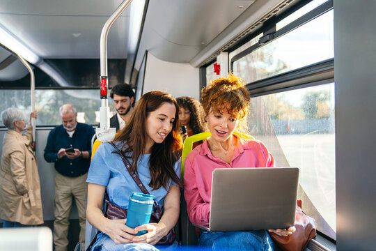 Passengers commuting on a bus, two women sharing a laptop screen while traveling, embracing technology and connectivity