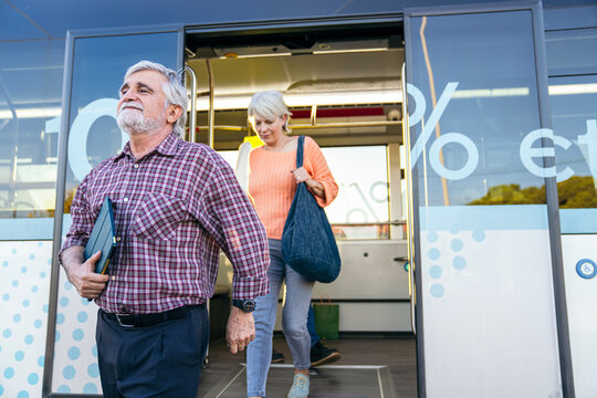 Elderly man and woman getting off a public city bus, using urban transport for their daily commute or leisure travel