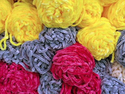 Colorful skeins of soft chenille yarn in yellow, gray, and red tones, close-up texture for knitting and craft backgrounds.