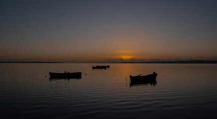 Boats silhouetted on calm water during colorful sunset horizon