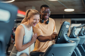 Smiling diverse young adults exercising together on treadmill in modern gym with bright lighting and fitness equipment