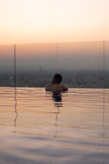Man relaxing in infinity pool watching muscat sunset