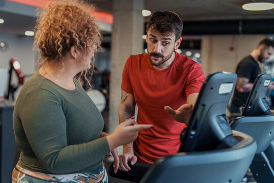 Curly haired woman and bearded man exercising together in modern gym using cardio machines - Powered by Adobe