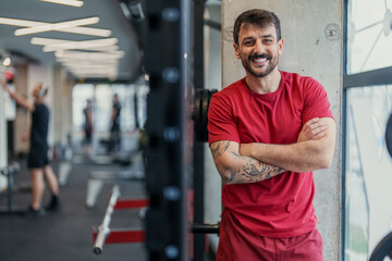 Obraz premium Smiling middle aged man in red athletic clothing standing confidently in gym with exercise equipment