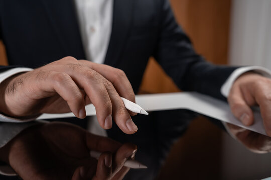 Close-up of businessman's hand touching digital pen on tablet in office setting, symbolizing technology and productivity in modern business concept.