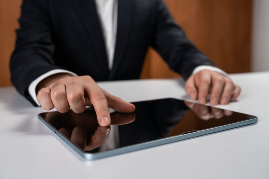 Businessman touching digital tablet screen with finger on desk in office environment, focusing on technology interaction concept in business context. - Powered by Adobe