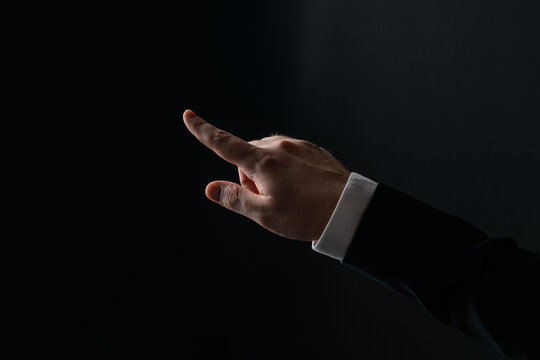 Businessman's hand pointing forward in a touch gesture on dark background, symbolizing technology interaction and innovation concept.