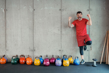 Energetic young man exercising in gym with colorful kettlebells and dumbbell near concrete wall
