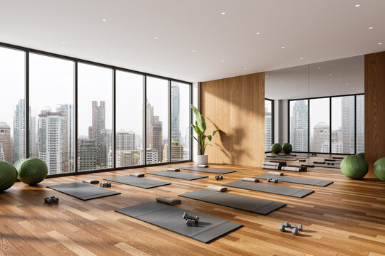 Modern yoga studio interior with panoramic city view, wooden flooring and minimalist design, featuring yoga mats, dumbbells and exercise balls. 3D Rendering