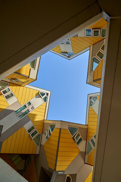 Looking up through a triangular opening in a modern building with yellow and white facades and unusual angles, the sky is clear and blue. Rotterdam, Holland.