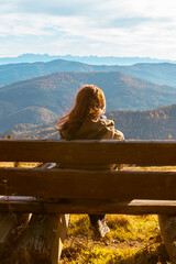 Girl sitting on a bench and enjoys the panorama of autumn mountains
