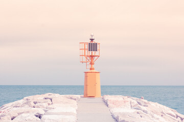 Small yellow lighthouse at the end of the pier against the blue sea
