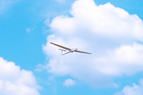 Small glider flying against the blue sky and clouds - Powered by Adobe
