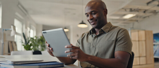 Focused Engagement: A professional individual is immersed in the details on a tablet in a well-lit modern workspace, showcasing his focused concentration.