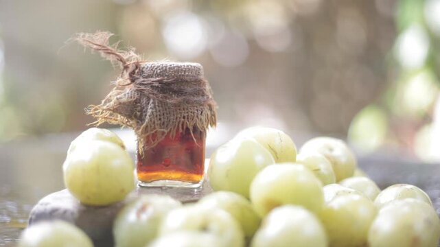 Close up of Indian gooseberry with its extracted essence or concentration in a transparent bottle on wooden surface with raw amla in a fruit and vegetable basket.