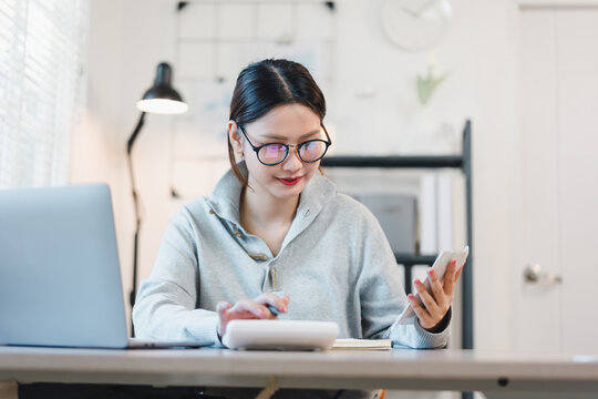 Focused young asian woman calculating finance and budget in home office, working with laptop and financial bills for her small business