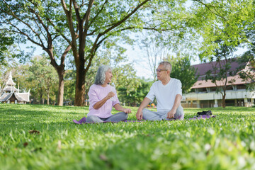 Happy Asian senior couple talking and relaxing during yoga meditation in green park. healthy lifestyle and wellness during retirement outdoor