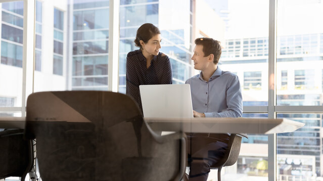 Two young diverse colleagues discuss online project on notebook screen