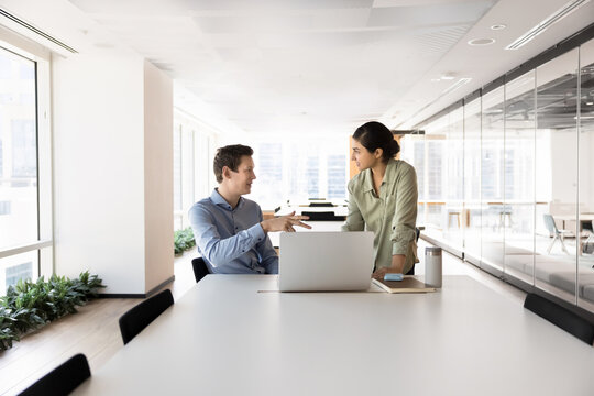 Two young diverse businesspeople teammates discuss research on notebook screen