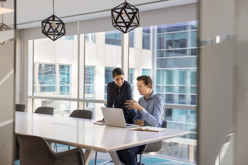Two young diverse businesspeople discuss paperwork using notebook at office