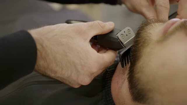 Professional barber trimming client's beard with trimmer. Clip