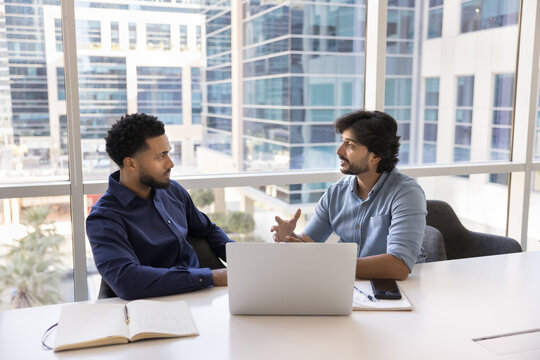 Matured male business professional mentoring millennial guy using notebook
