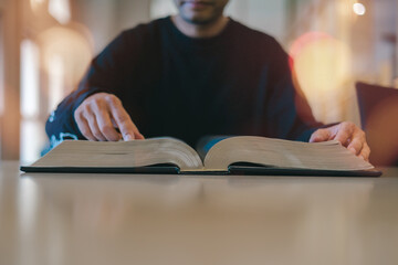 Person reading a large open book on a table in library or study room, representing research, knowledge, academic study, and learning. Ideal for education, literature research-related content.