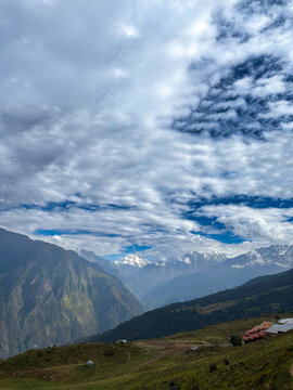 Wide Vista of Auli Slopes with Resort Structures and Majestic Snow Peaks under Dynamic Cloudy Sky.