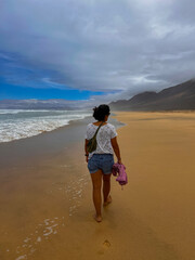 Young Woman Walking on Cofete Beach, Fuerteventura, with Backpack on a Sunny Cloudy Day