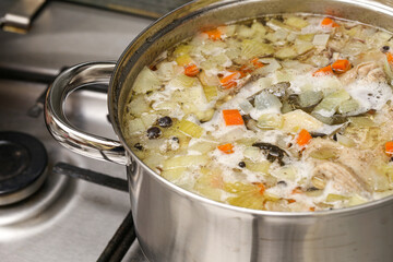 Large pot with homemade soup boiling on stove. Fresh vegetables and meat cooking in hot broth. Concept of traditional cuisine, comfort food, and homemade meal.